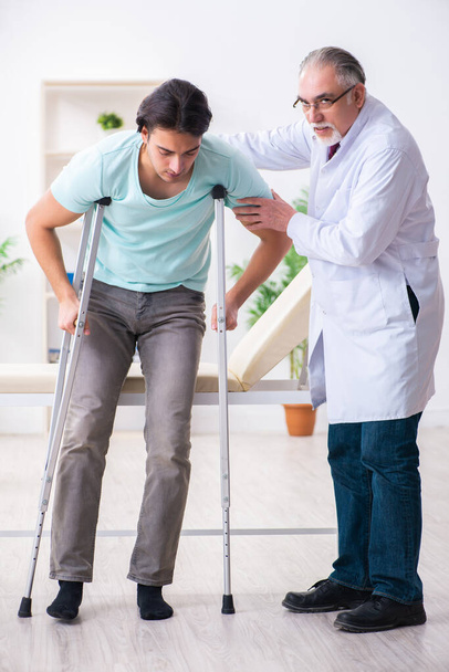 Νεαρός τραυματισμένος άνδρας ασθενής που επισκέπτεται ηλικιωμένο γιατρό - Φωτογραφία, εικόνα
