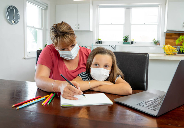 Coronavirus Outbreak. Lockdown and school closures. Mother helping bored daughter with face mask studying online classes at home. COVID-19 pandemic forces children and teachers online learning. - Valokuva, kuva