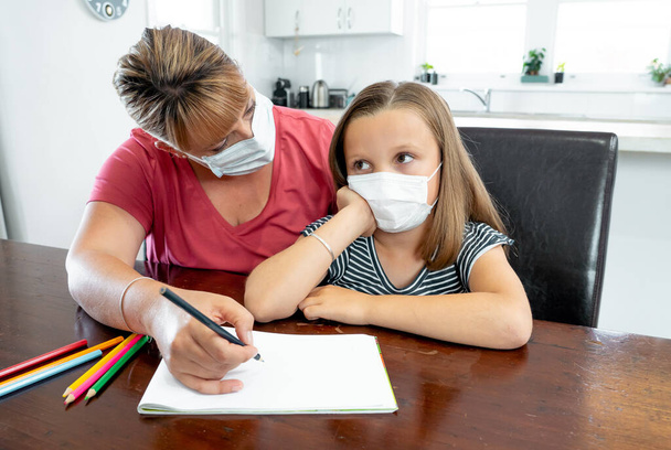 Coronavirus Outbreak. Lockdown and school closures. Mother helping bored daughter with face mask studying online classes at home. COVID-19 pandemic forces children and teachers online learning. - Photo, Image