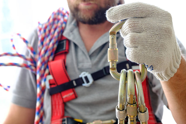 un homme en équipement pour le travail en altitude tient un tas de mousquetons dans sa main pour fixer l'équipement. respect des règles de travail conformément à la protection du travail en hauteur
 - Photo, image