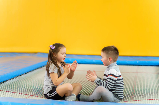 Feliz sorrindo crianças pequenas sentadas no trampolim interior e jogando no centro de entretenimento
 - Foto, Imagem