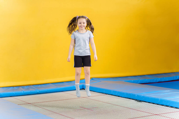 Happy little girl jumping on trampoline in fitness center - Photo, Image