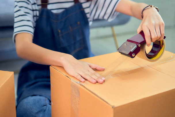 Startup small business concept, young Asian woman owner working and packing on the box to customer at the sofa in home office, seller prepares the delivery. - Foto, Bild