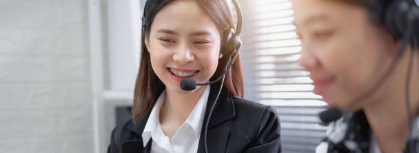 Smiling Asian woman consultant wearing microphone headset of customer support phone operator at workplace. - Photo, image
