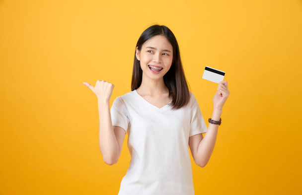 Houkutteleva hymyilevä aasialainen nainen, jolla on luottokorttimaksu keltaisella taustalla kopiointitilalla. - Valokuva, kuva