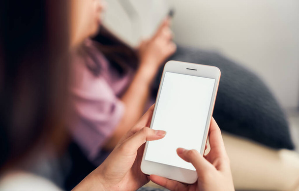Frau hält Smartphone mit leerem Bildschirm auf Sofa im Haus mit Freunden. Nehmen Sie Ihren Bildschirm, um Werbung zu schalten. - Foto, Bild