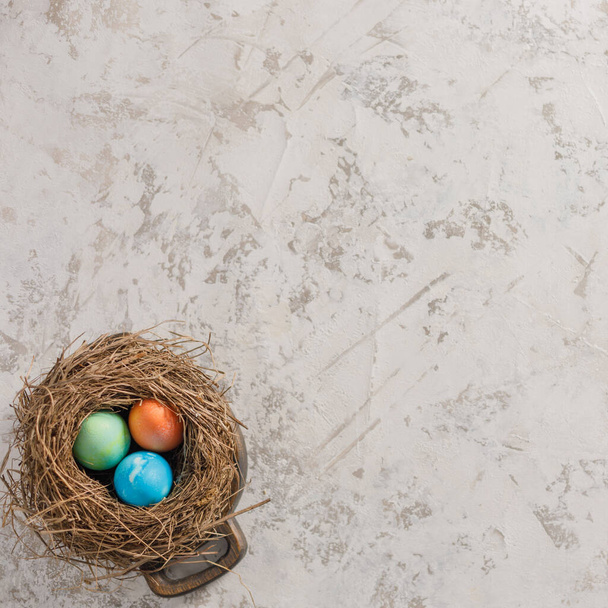 Easter eggs in a bird's nest on a textural background. Easter celebration concept. Copy space. Flat lay. - Фото, изображение