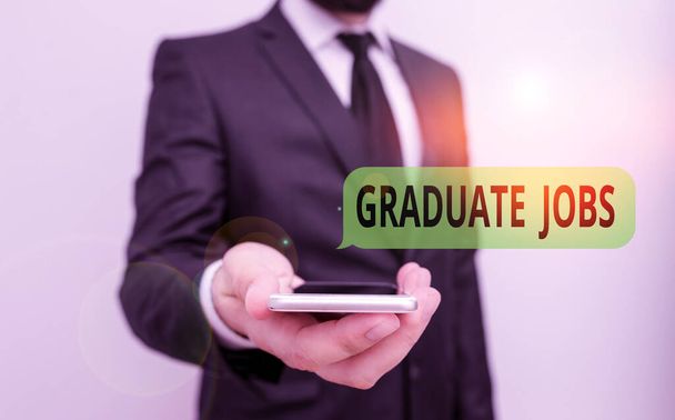 Word writing text Graduate Jobs. Business concept for require someone to hold a degree to start their career Male human wear formal work suit hold smart hi tech smartphone use one hand. - Photo, Image