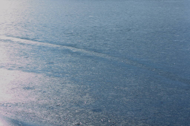 frozen lake on a clear winter day, covered with blue ice , which reflects the sun's glare. - Photo, Image