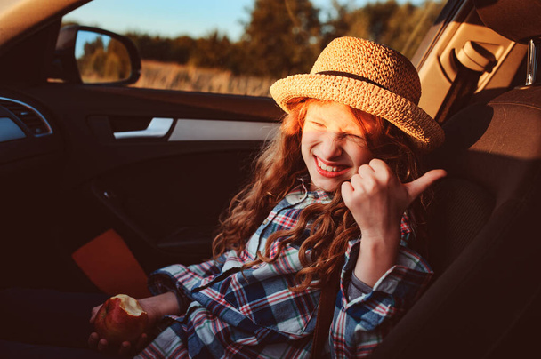 happy child girl eating apple in car. Summer road trip concept, lifestyle shot - Photo, Image