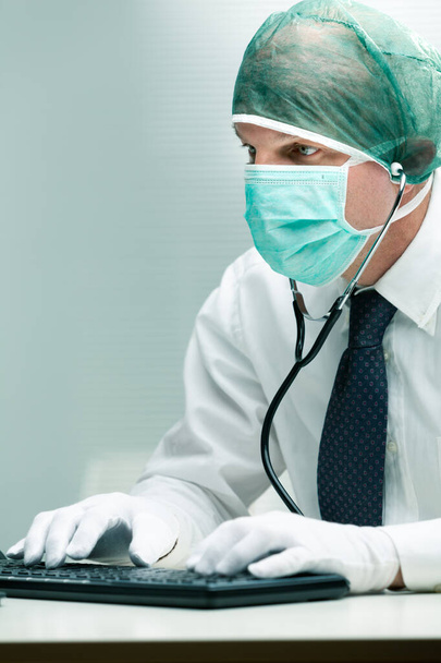 office worker using mask gloves and a stethoscope while typing on a computer keyboard - Photo, Image
