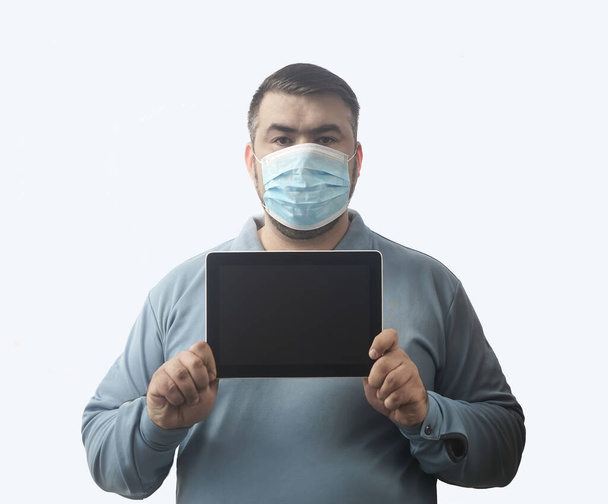 Man with mask to protect him from Coronavirus. Corona virus pandemic. Man hold  mask before face. Young man with mask standing. Person in hood with medical mask. isolated on white background. tablet computer in hands. empty screen frame. - Fotografie, Obrázek