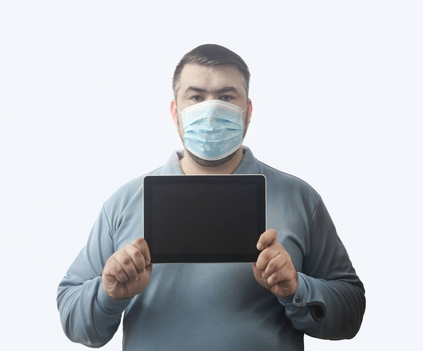 Man with mask to protect him from Coronavirus. Corona virus pandemic. Man hold  mask before face. Young man with mask standing. Person in hood with medical mask. isolated on white background. tablet computer in hands. empty screen frame. - Photo, Image