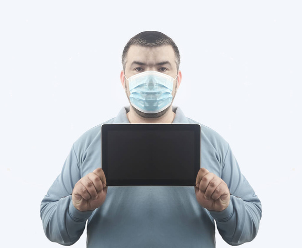 Man with mask to protect him from Coronavirus. Corona virus pandemic. Man hold  mask before face. Young man with mask standing. Person in hood with medical mask. isolated on white background. tablet computer in hands. empty screen frame. - Photo, Image