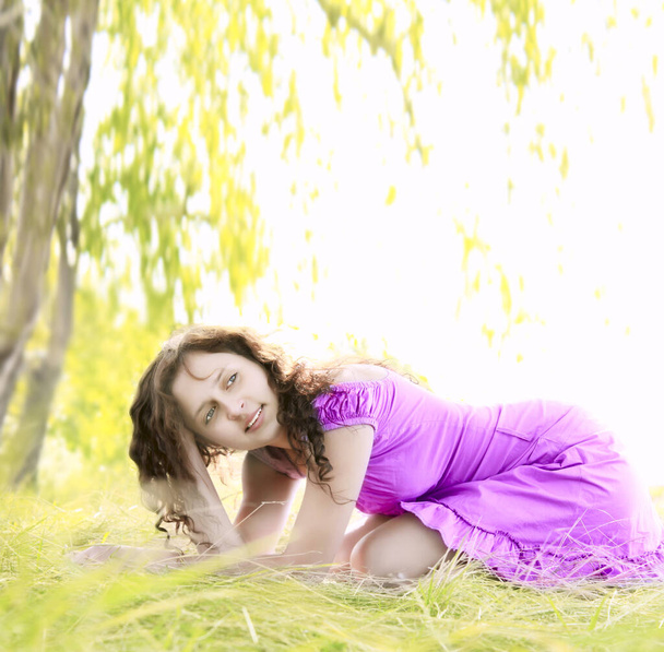 Молодая рыжая женщина в фиолетовом платье, летом сидит на зеленом травяном лугу. весенний сезон
.  - Фото, изображение