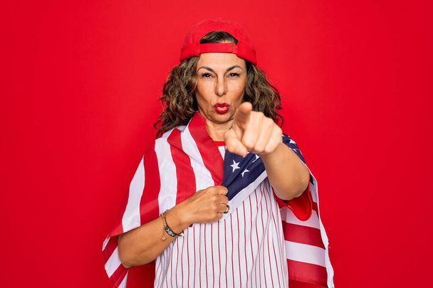 Orta yaşlı, vatansever, beyzbol ekipmanı takan, elinde kameraya işaret eden Amerikan bayrağı tutan yaşlı bir kadın ve sen, el işareti, ön taraftan olumlu ve kendinden emin bir jest. - Fotoğraf, Görsel