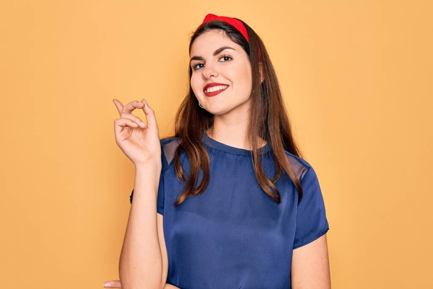 Young beautiful brunette woman wearing red lips over yellow background with a big smile on face, pointing with hand and finger to the side looking at the camera. - Fotó, kép