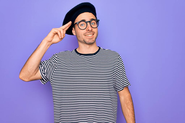 Handsome man with blue eyes wearing striped t-shirt and french beret over purple background Smiling pointing to head with one finger, great idea or thought, good memory - Photo, image