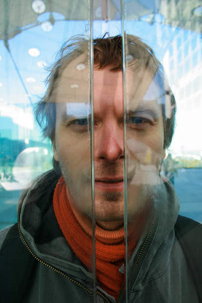 Portret van jonge shaggy man met blauwe ogen gluren door een sleuf tussen dikke glazen. - Foto, afbeelding