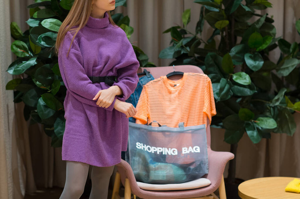 Mujer joven estancia relajante y bolsa de compras y ropa en la tienda
 - Foto, Imagen