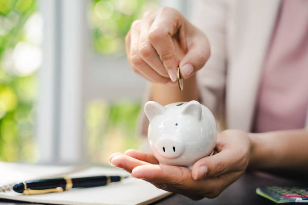 Closeup of business woman hand putting money coin into piggy bank for saving money. saving money and financial concept - Photo, Image
