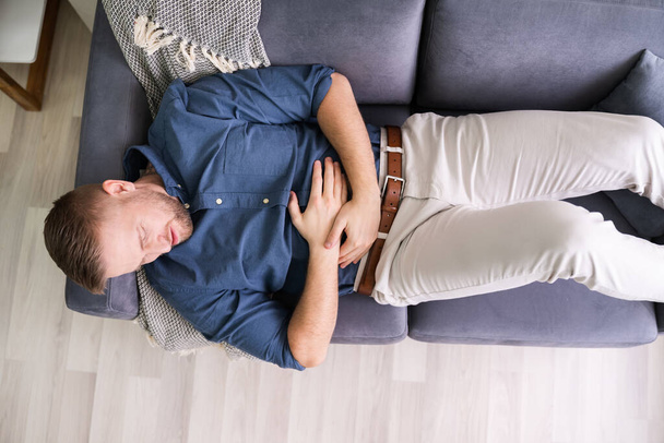 Man Suffering From Stomach Ache Lying On Sofa - Foto, Bild