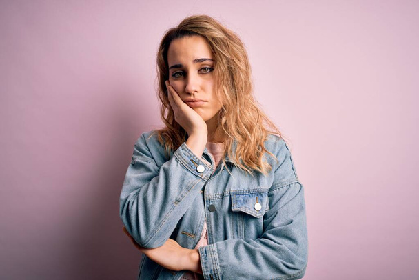 Young beautiful blonde woman wearing casual denim jacket standing over pink background thinking looking tired and bored with depression problems with crossed arms. - Photo, Image