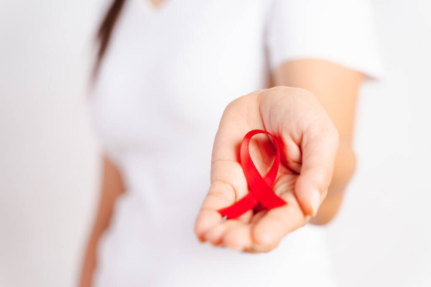 Closeup woman hand holding red ribbon HIV, world AIDS day awareness ribbon. Healthcare and medicine concept. - Photo, Image