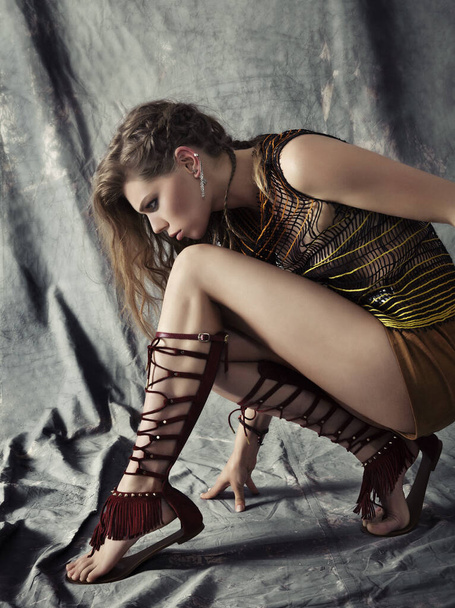 beautiful woman crouching in long tassel sandals and short shorts. - Foto, afbeelding