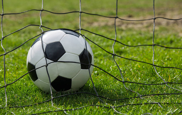 Κοντινό πλάνο μιας μπάλας ποδοσφαίρου πίσω από τις πύλες καθαρό, την έννοια της βαθμολόγησης γκολ. Εξωτερικός ποδοσφαιρικός αγώνας, εξάσκηση σε ανοιξιάτικα αθλήματα. Υγιεινή δραστηριότητα και παιχνίδια, πράσινο φόντο χλοοτάπητα. - Φωτογραφία, εικόνα