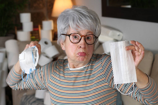 Doubtful senior woman holding two types of masks - Фото, зображення