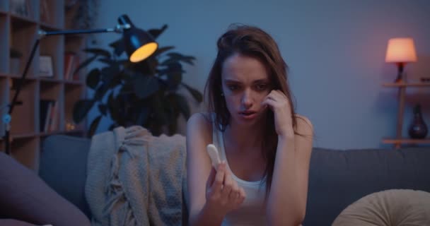 Shocked unhappy girl finding out about having baby and covering face with hands. Young woman sitting on sofa and worrying about unwanted pregnancy. Concept of fear and unplaned pregnancy. - Footage, Video