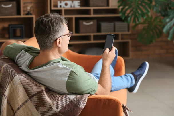 Mature man with mobile phone at home - Foto, Bild