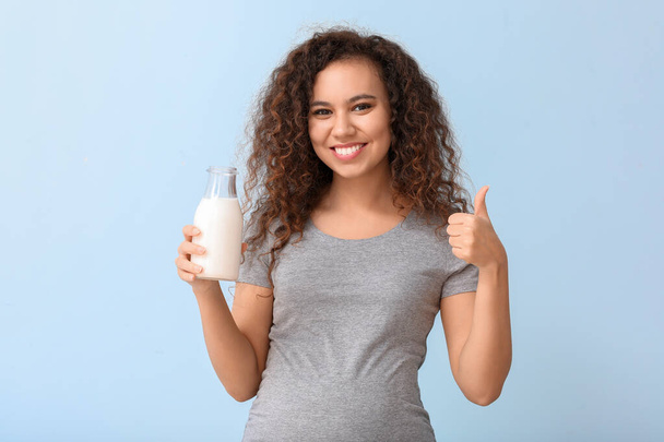 Mujer afro-americana embarazada joven con leche sobre fondo de color
 - Foto, imagen