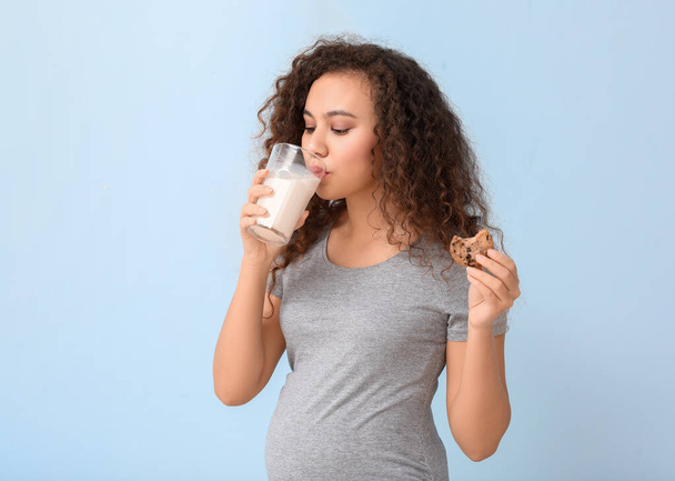 Young pregnant African-American woman with milk and cookie on color background - Photo, Image