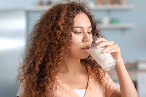 Genç Afro-Amerikalı kadın mutfakta süt içiyor. - Fotoğraf, Görsel