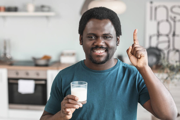 Sütlü ve işaret parmağıyla mutfakta genç bir Afro-Amerikalı. - Fotoğraf, Görsel