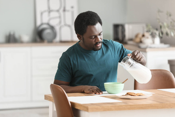 Young African-American man with milk and flakes in kitchen - Φωτογραφία, εικόνα