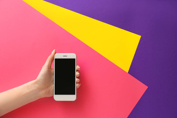 Vrouwelijke hand met mobiele telefoon op kleur achtergrond - Foto, afbeelding