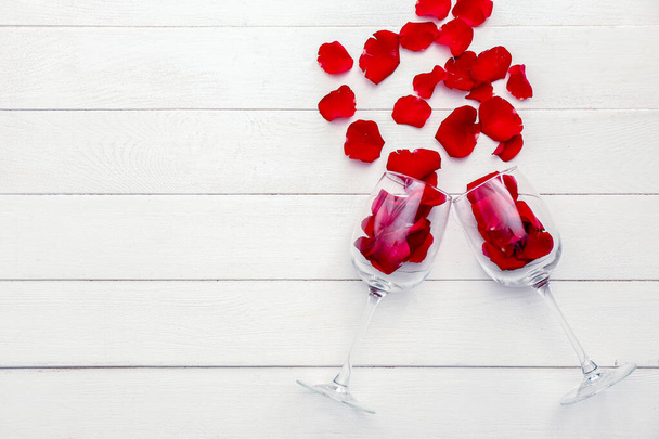 Wineglasses with rose petals on white wooden background - Photo, Image