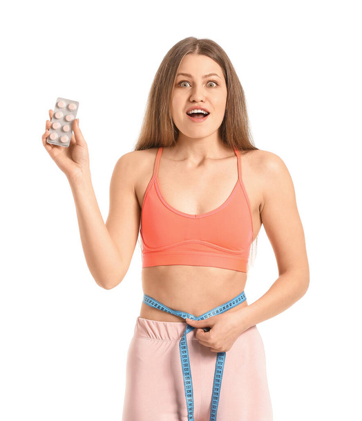 Young woman with weight loss pills and measuring tape on white background - Foto, Imagen
