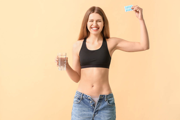 Woman in loose jeans and with weight loss pills on color background - Photo, Image