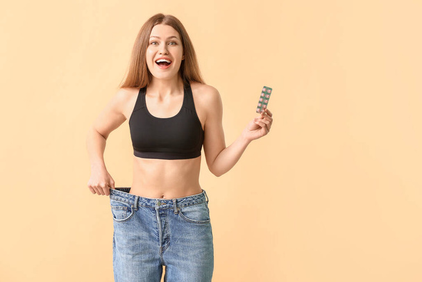 Woman in loose jeans and with weight loss pills on color background - Φωτογραφία, εικόνα