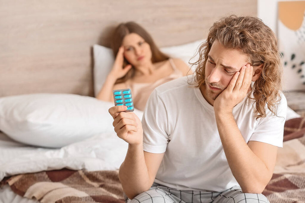 Droevige man met orale erectiestoornissen medicatie en zijn vrouw in de slaapkamer - Foto, afbeelding