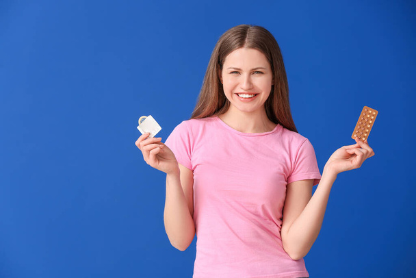 Młoda kobieta z pigułek antykoncepcyjnych i prezerwatywy na tle koloru - Zdjęcie, obraz