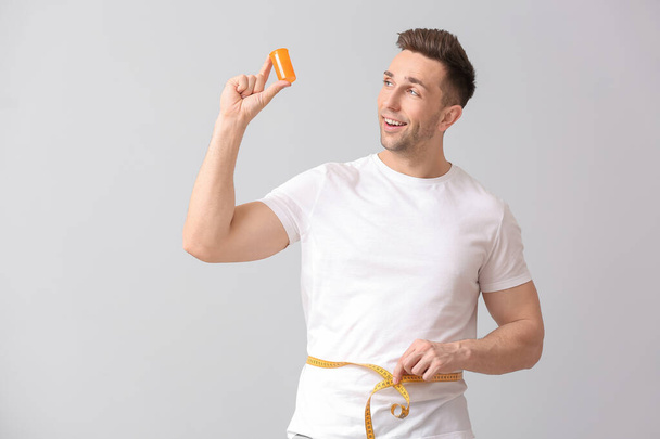 Young man with weight loss pills and measuring tape on light background - Foto, Imagen