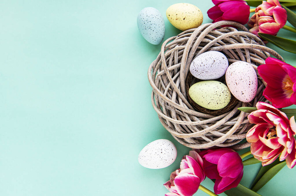 Easter background with colorful eggs in nest and pink tulips on a pastel green background. Top view with copy space - Φωτογραφία, εικόνα