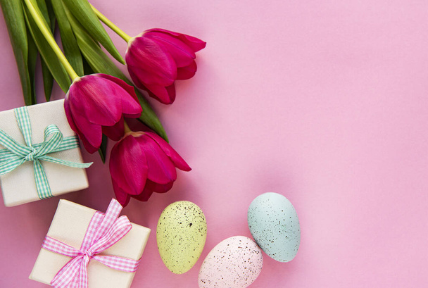Jarní tulipánové květiny, velikonoční vajíčka a dárková krabice na pastelově růžovém pozadí. Pozdrav na Velikonoce. Pohled shora, byt ležel. - Fotografie, Obrázek