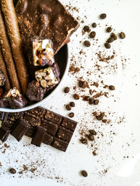Different chocolate bars, chocolates, chocolate tubes sprinkled with cocoa on the table and in a white plate - Fotografie, Obrázek