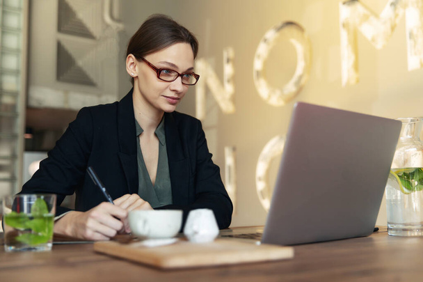 La donna d'affari focalizzata in occhiali eleganti si siede su caffè che lavora su computer portatile, la femmina seria concentrata che lavora con computer e cappuccino in caffetteria, il collaboratore esterno, studiando in linea, naviga Internet, controllando conti
 - Foto, immagini